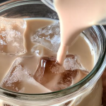 Iced English tea latte in a clear glass with lemon and mint garnish on a wooden table.