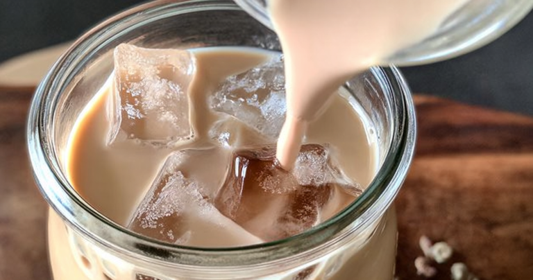 Iced English tea latte in a clear glass with lemon and mint garnish on a wooden table.