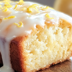 Slice of Starbucks-inspired lemon loaf with glaze and lemon zest on a wooden board