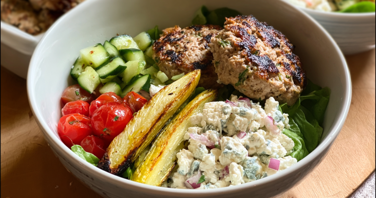 Mediterranean turkey burger bowl with roasted potatoes and hummus on a wooden table.