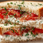 Freshly made tomato sandwich on whole wheat bread with herbs on a wooden cutting board.