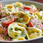 Bowl of fresh grinder tortellini salad with grape tomatoes and pepperoncini on a wooden table.