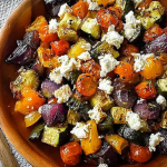 Plate of roasted vegetables with feta cheese on a wooden table.