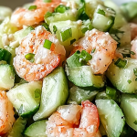 A vibrant cucumber shrimp salad with dill and lime on a wooden table, showcasing fresh ingredients and a creamy dressing.