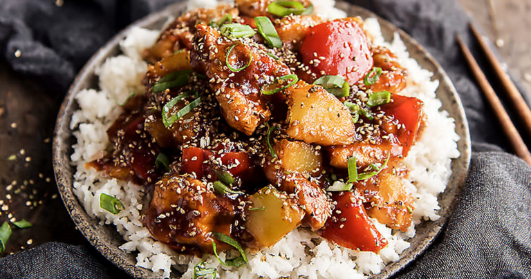 Sweet Hawaiian Crockpot Chicken served over rice with green onions and sesame seeds in a tropical setting.