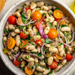 Italian white bean salad with cherry tomatoes and olives in a rustic bowl next to a slice of crusty bread