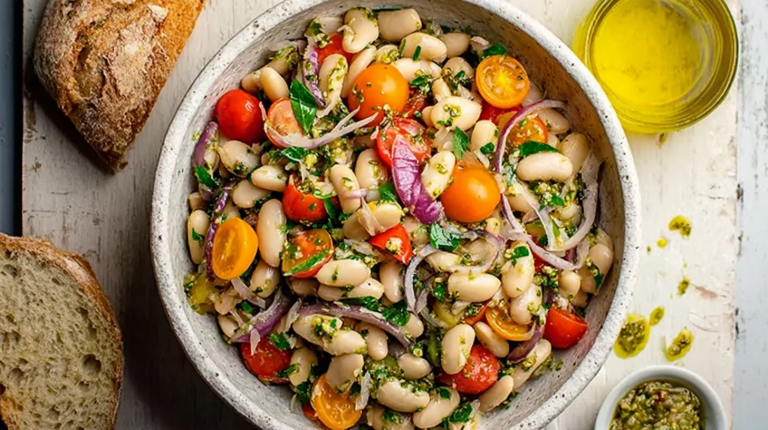 Italian white bean salad with cherry tomatoes and olives in a rustic bowl next to a slice of crusty bread