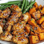Plated honey garlic chicken with roasted sweet potatoes and green beans, garnished with herbs.