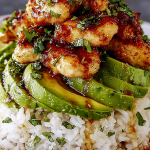 Gluten-free tangy honey lime chicken layered over avocado rice, garnished with fresh cilantro and lime slices on a wooden table.
