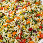 Rainbow orzo salad with colorful vegetables served in a bowl on a wooden table.