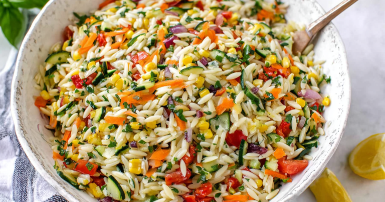 Rainbow orzo salad with colorful vegetables served in a bowl on a wooden table.