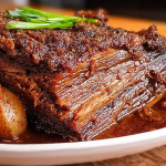 Close-up of sliced slow cooked beef brisket on a wooden cutting board, garnished with herbs.