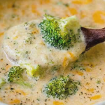 Creamy broccoli cheddar soup topped with shredded cheese in a rustic bowl, surrounded by fresh broccoli florets.
