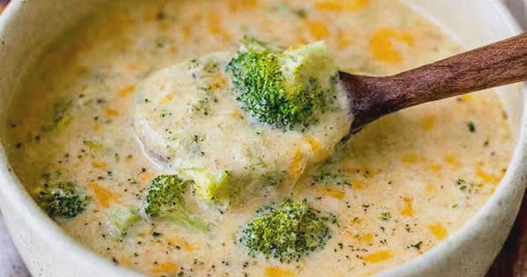 Creamy broccoli cheddar soup topped with shredded cheese in a rustic bowl, surrounded by fresh broccoli florets.
