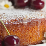 Sliced cherry almond cake with bright cherries and almond glaze on a cake stand.