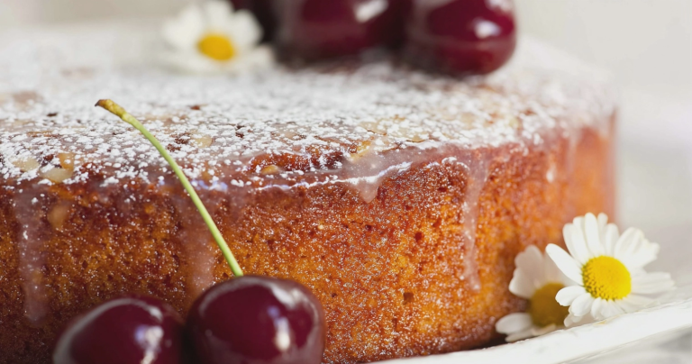 Sliced cherry almond cake with bright cherries and almond glaze on a cake stand.