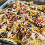 Close-up of creamy slow cooker chicken nachos garnished with cilantro on a wooden table.