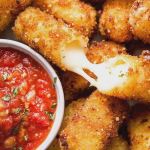 Crispy homemade mozzarella sticks with marinara sauce and fresh basil on a wooden platter.