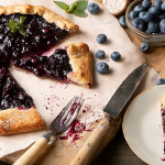Homemade blueberry galette displayed on a rustic wooden table with fresh blueberries around it, showcasing the delicious filling and flaky crust.