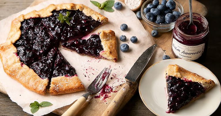 Homemade blueberry galette displayed on a rustic wooden table with fresh blueberries around it, showcasing the delicious filling and flaky crust.