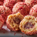 Close-up of strawberry crunch protein bites on a plate with fresh strawberries, highlighting their red and white layers.