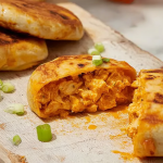 Golden-brown buffalo chicken hot pockets with chives on a wooden table, served with a bowl of dipping sauce.