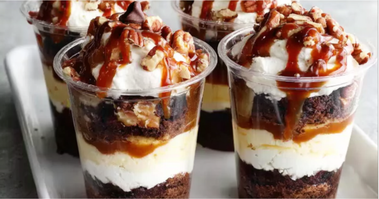 Loaded Brownie Cheesecake Cups with chocolate ganache and caramel drizzle on a wooden table.
