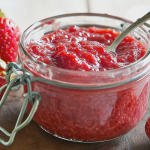 Homemade sugar free strawberry jam in a jar with fresh strawberries and a wooden spoon.