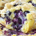 Freshly baked lemon blueberry muffins with blueberries and lemon slices on a wooden table.