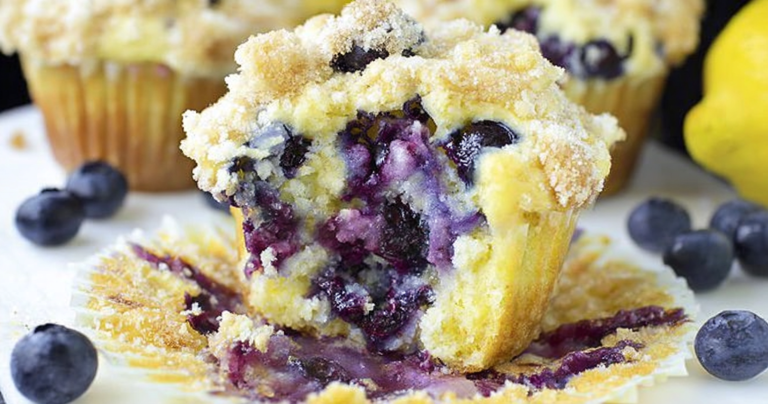 Freshly baked lemon blueberry muffins with blueberries and lemon slices on a wooden table.
