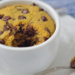 Close-up of a chocolate chip mug cookie topped with vanilla ice cream in a mug on a wooden table.