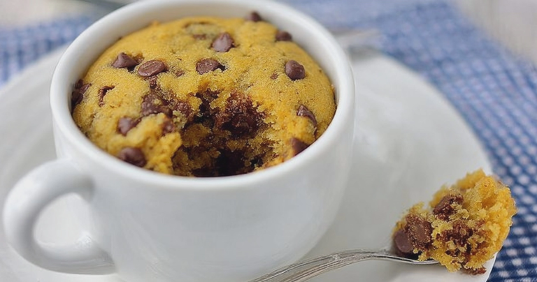 Close-up of a chocolate chip mug cookie topped with vanilla ice cream in a mug on a wooden table.