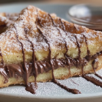 Close-up of golden Nutella toast pies with powdered sugar and fresh strawberries on a plate.