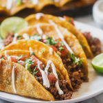Close-up of crispy beef tacos filled with seasoned ground beef and melted cheddar cheese, garnished with salsa.