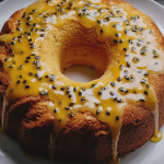 Slice of mango coconut cake with passionfruit glaze on a decorative plate surrounded by coconut flakes and mango slices.