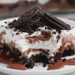 Slice of no bake chocolate lasagna on a wooden table, highlighting layers of Oreo crust, cream cheese filling, chocolate pudding, and chocolate chips.