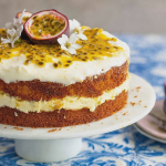 Slice of moist passion fruit cake garnished with fresh passion fruit and mini meringues on a wooden table.
