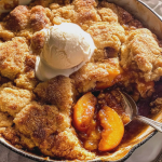 Freshly baked caramel peach dump cake with ice cream and mint leaves on a wooden table.