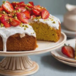 Slice of strawberry pistachio olive oil cake topped with whipped cream and fresh strawberries on a wooden table
